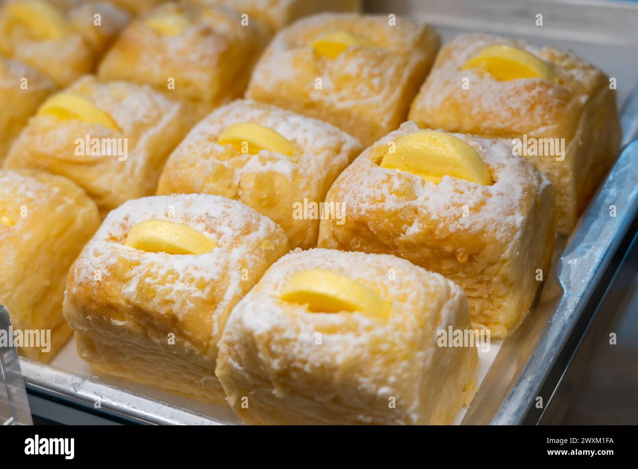 Panini lussureggianti cosparsi di zucchero a velo e un pezzo di burro, frutta e formaggio, bellissimi in una finestra di panetteria. Foto Stock