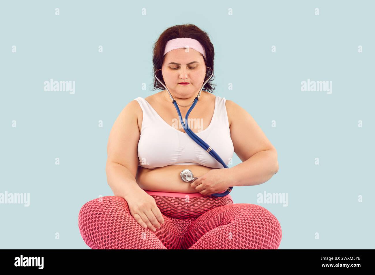 La donna obesa in sovrappeso tiene lo stetoscopio sulla pancia grassa e ascolta i suoni intestinali Foto Stock