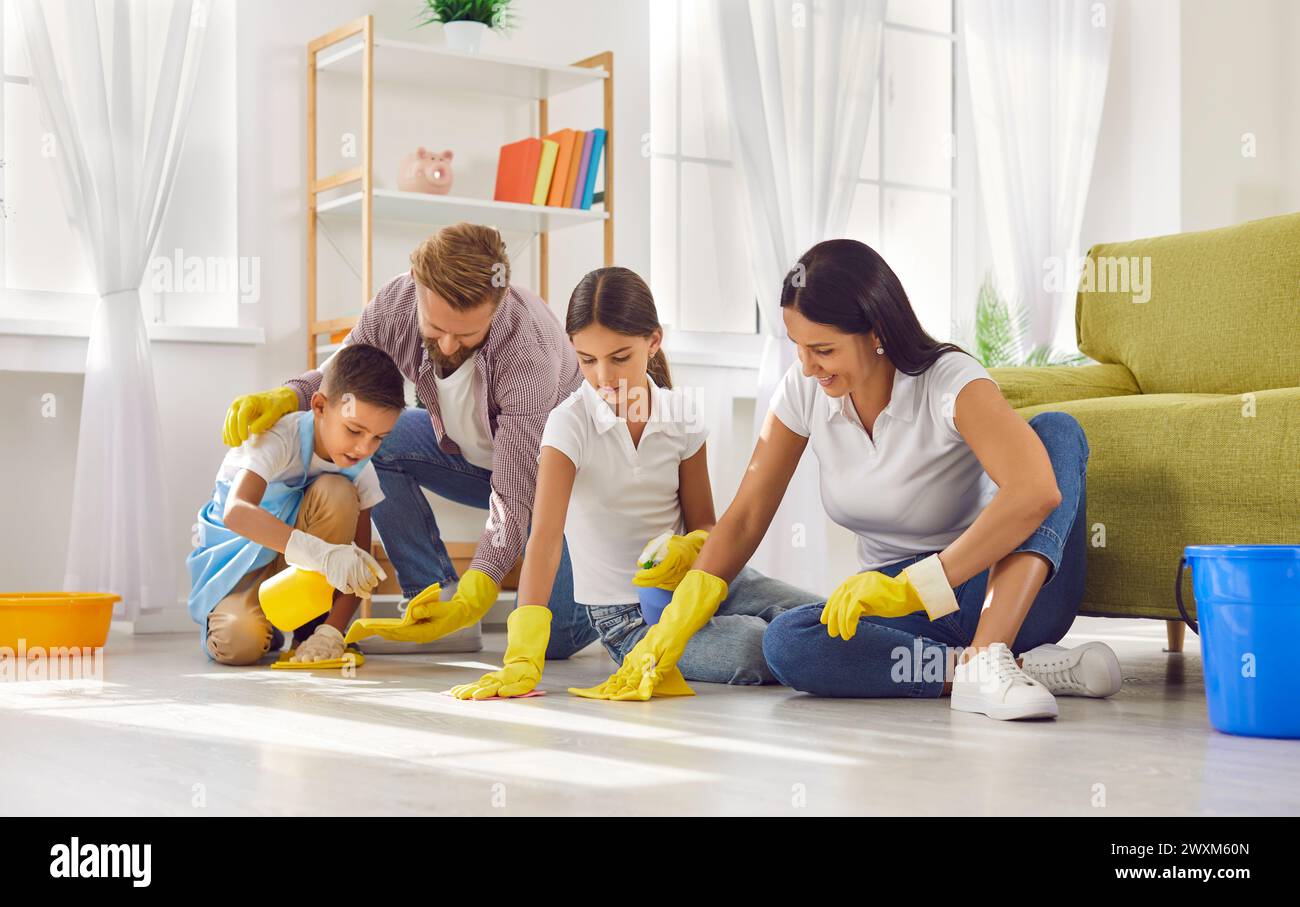 Genitori piccoli con bambini che puliscono il pavimento insieme nel soggiorno di casa Foto Stock
