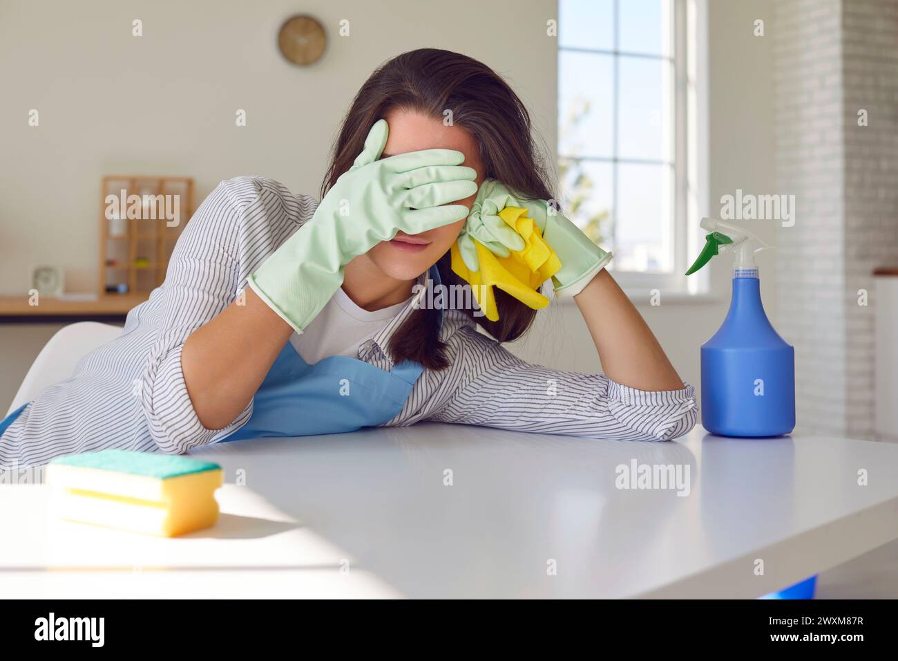 Donna stanca casalinga con strumenti di pulizia in piedi in cucina e coprire il viso con le mani. Foto Stock