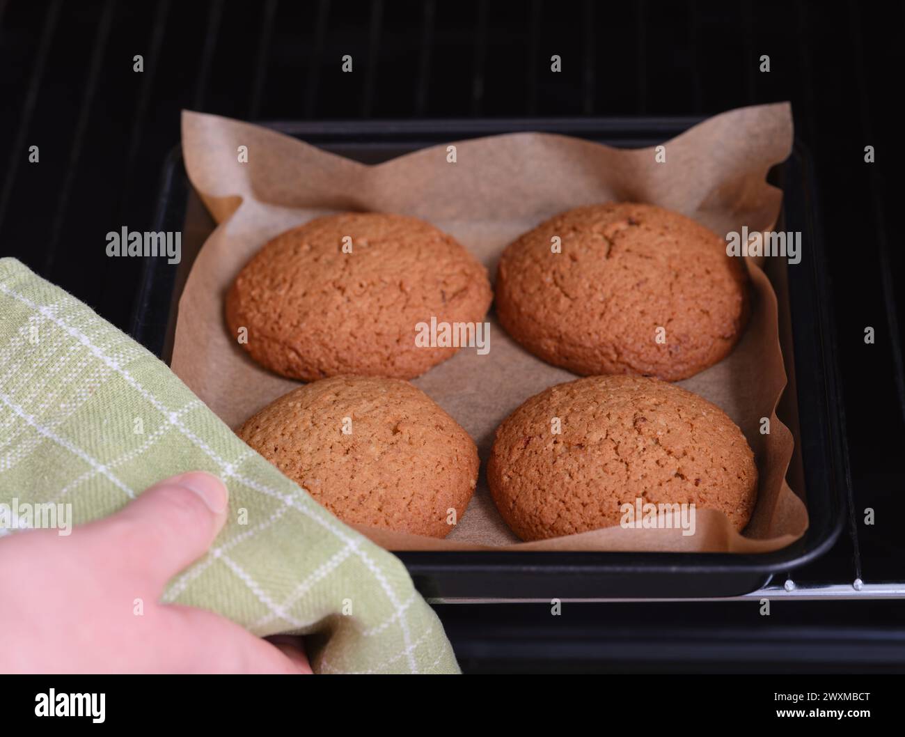 Una donna che prende un vassoio da forno con quattro biscotti d'avena. Foto Stock