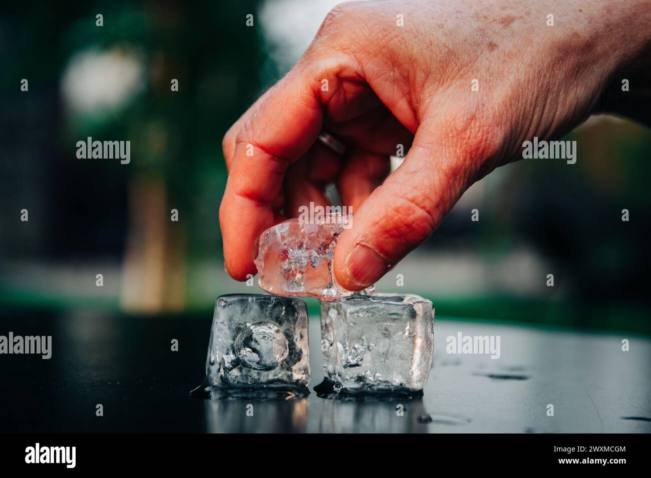 Una mano che impila tre cubetti di ghiaccio uno sopra l'altro Foto Stock