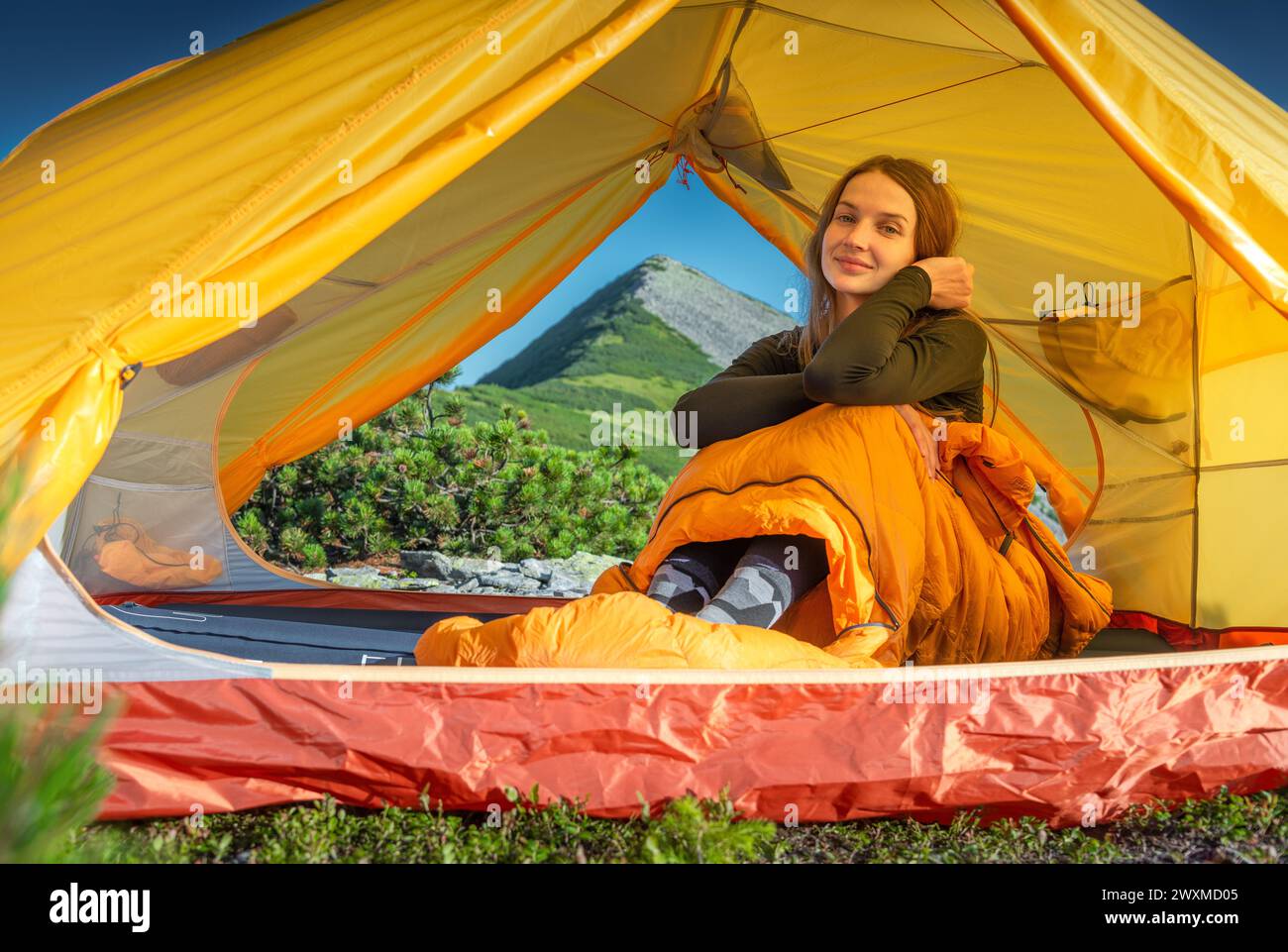 Giovane donna seduta nel sacco a pelo nella sua tenda Foto Stock