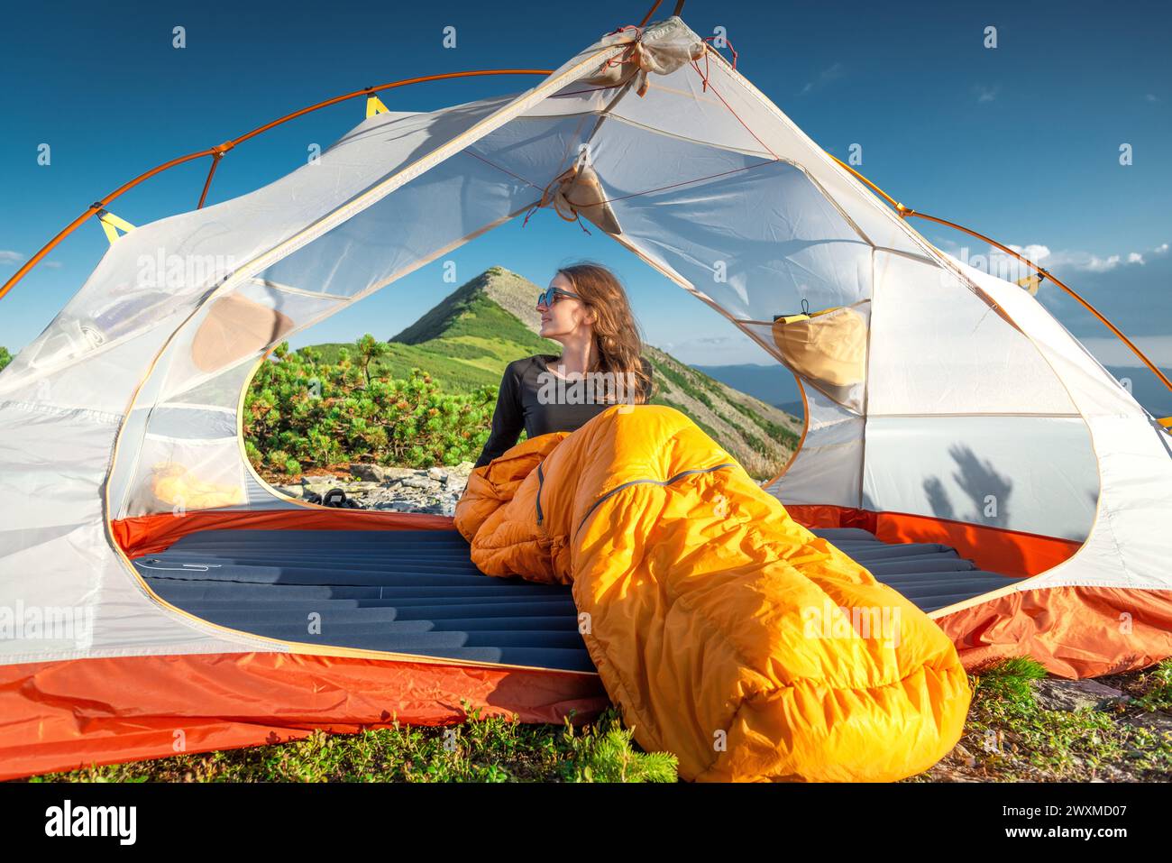 Giovane donna in sacco a pelo che guarda Sunsete dalla sua tenda Foto Stock