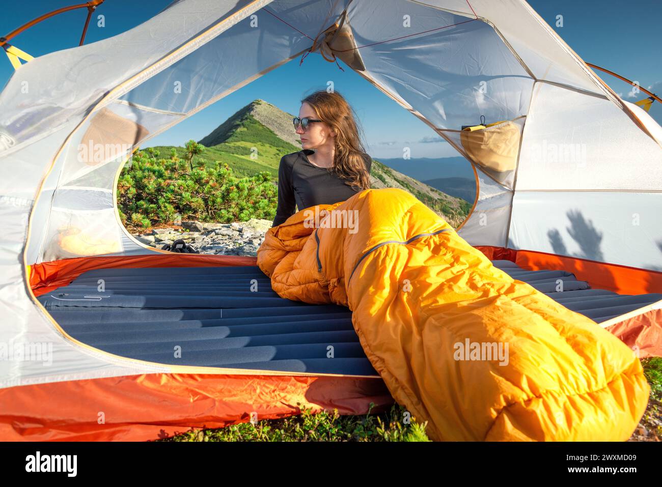 Giovane donna in sacco a pelo che guarda Sunsete dalla sua tenda Foto Stock