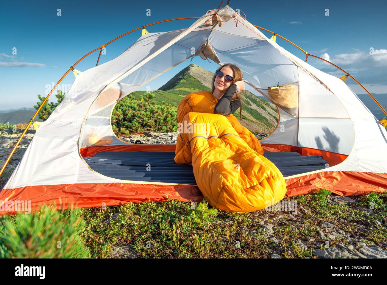 Giovane donna seduta nel sacco a pelo nella sua tenda Foto Stock