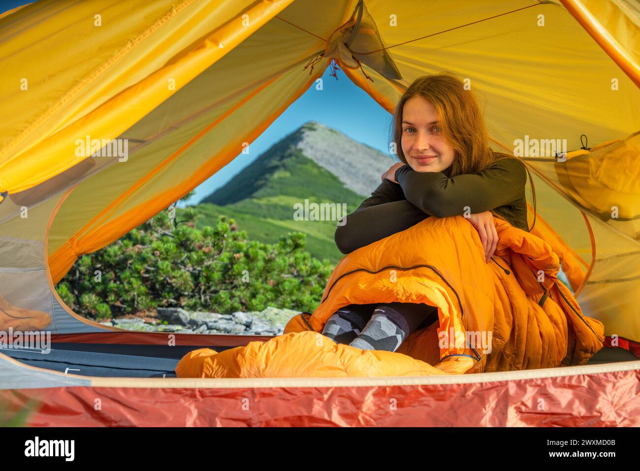 Giovane donna seduta nel sacco a pelo nella sua tenda Foto Stock