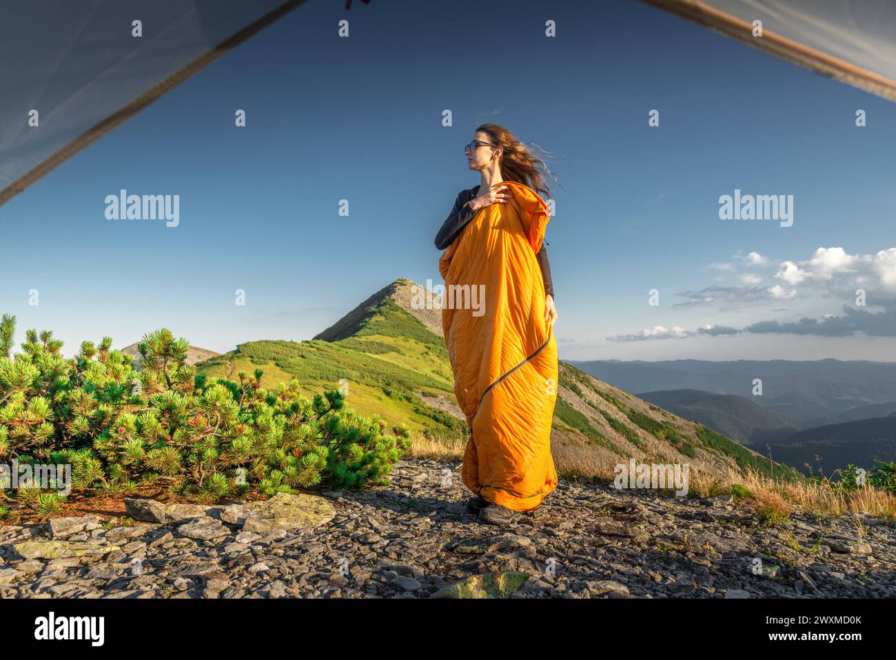Donna in piedi nel sacco a pelo accanto alla sua tenda su una montagna Foto Stock