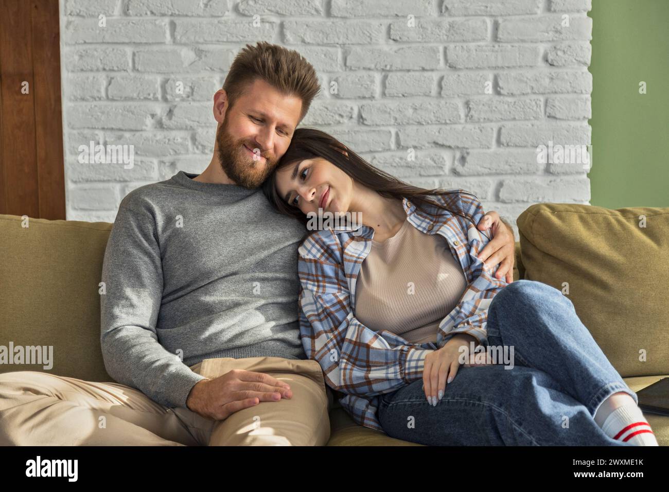 la coppia d'amore si siede sul divano insieme rilassandosi, coccolandosi e abbracciando Foto Stock