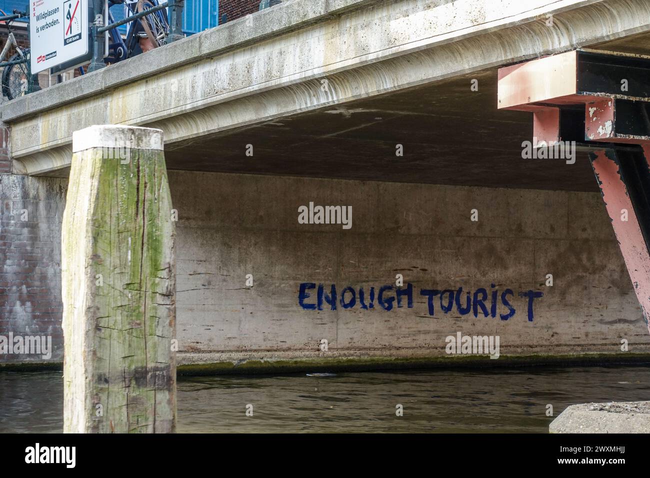 Graffiti che recitano "ABBASTANZA TURISTI" sotto un ponte sul canale con le biciclette parcheggiate sopra, mostrando il sentimento stufo di Amsterdam con il turismo nel centro della città Foto Stock