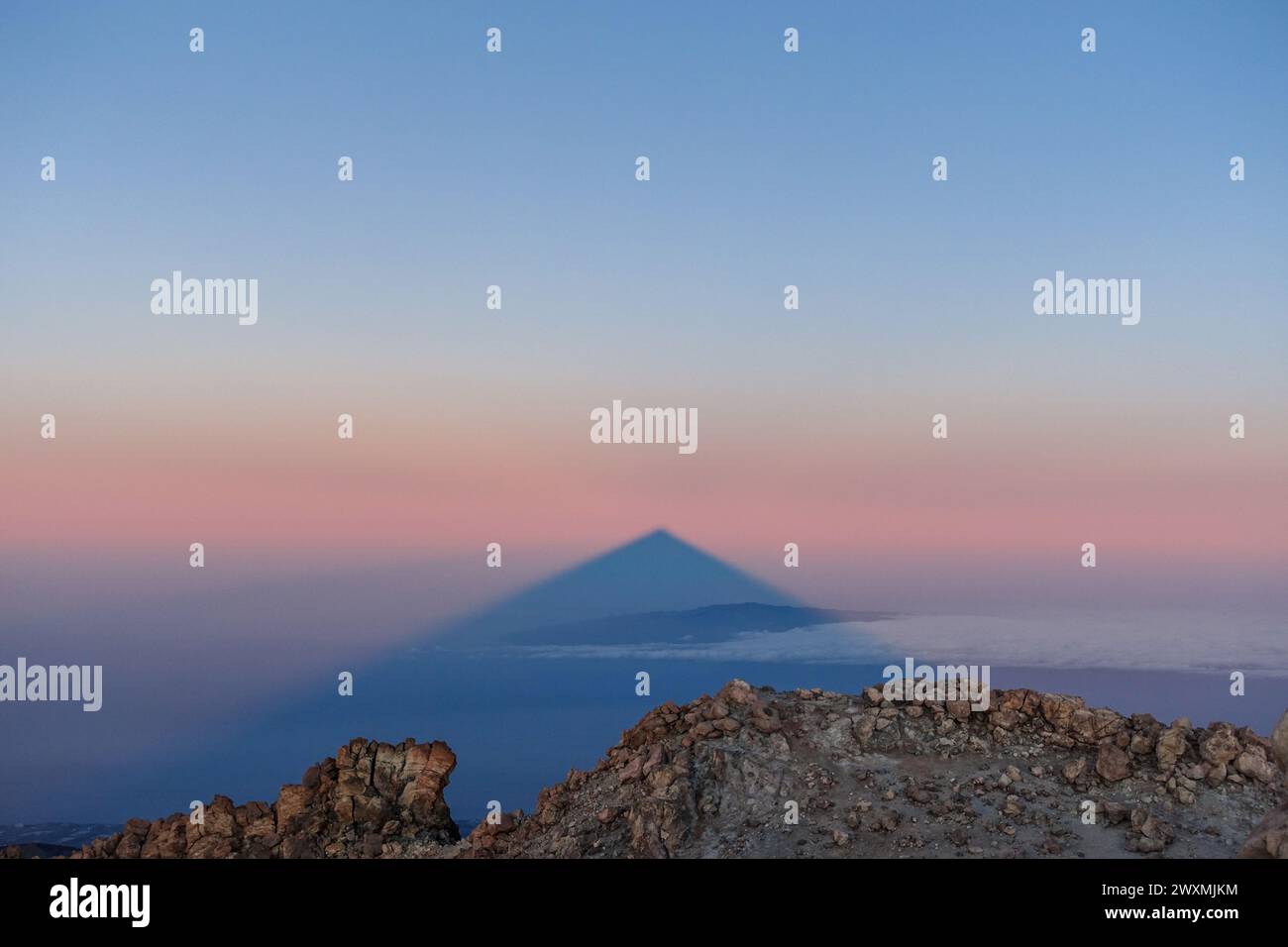 Vulcano Teide che getta una grande ombra triangolare su un cielo color pastello e uno strato di nuvole all'alba, Tenerife Foto Stock