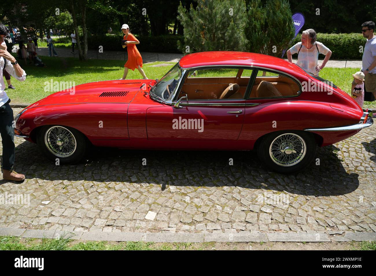 Una classica Jaguar e-Type rossa parcheggiata su una strada acciottolata circondata da persone Foto Stock