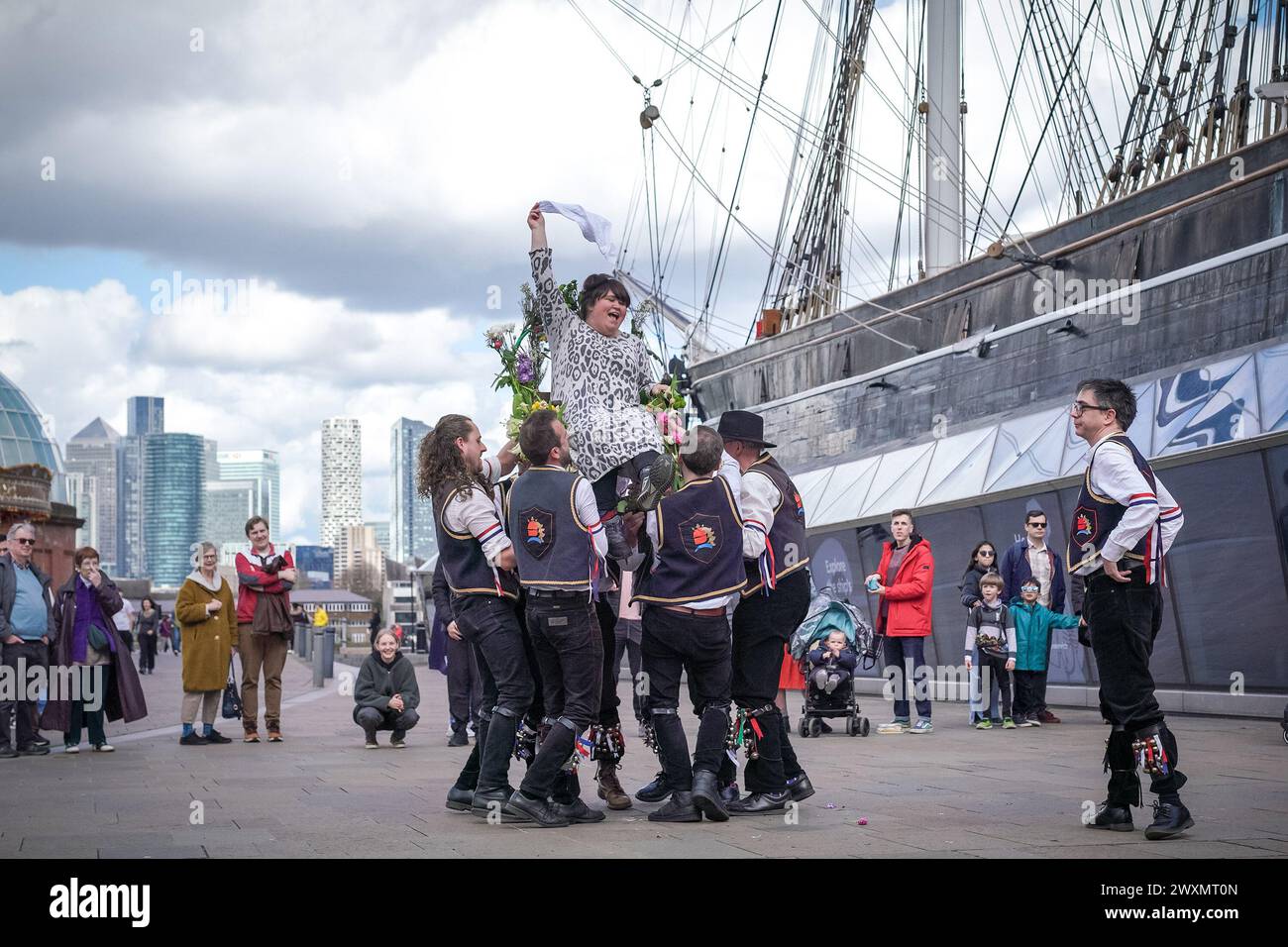 Londra, Regno Unito. 1 aprile 2024. La tradizione di sollevamento della sedia pasquale di Blackheath Morris Men vicino alla nave Cutty Sark a Greenwich. Una signora locale viene sollevata (o salutata) e trasformata tre volte da Morris Men mentre si siede su una sedia da pub decorata festosamente con fiori primaverili. Appartenente ad una tradizione più antica, essendo una forma di sacrificio a Eostre, un'antica dea della primavera che è strettamente associata alle celebrazioni pasquali pagane originali. Crediti: Guy Corbishley/Alamy Live News Foto Stock