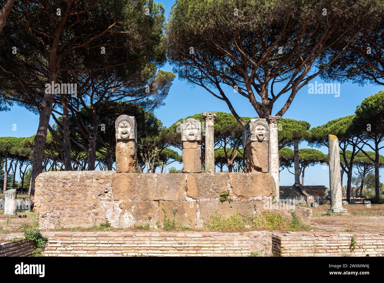 Maschere teatrali maschili scolpite su blocchi di marmo sostenuti da pilastri nelle rovine del parco archeologico nell'antica Ostia Foto Stock