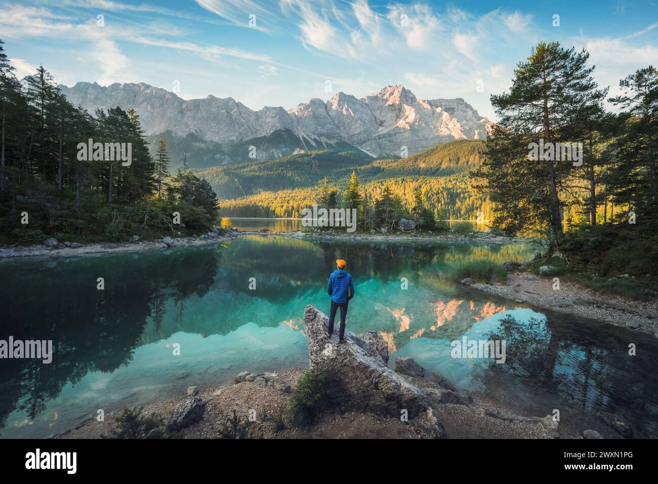 Uomo che si gode l'incredibile paesaggio mattutino in uno splendido lago delle Alpi Bavaresi, con acqua color acqua verde acqua che riflette la vista della catena montuosa e del ni Foto Stock