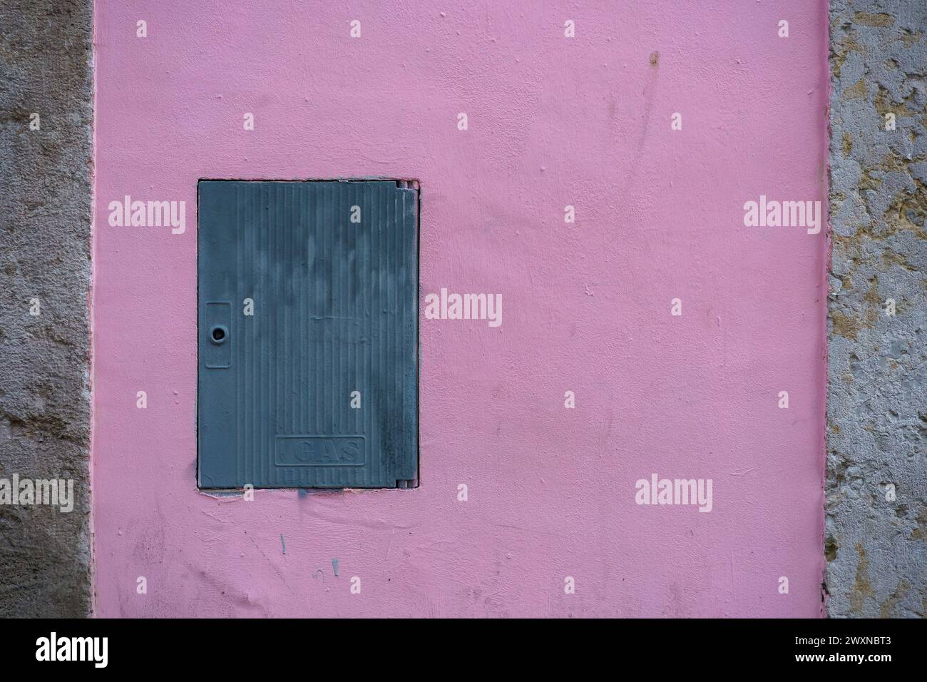 Piccola porta metallica blu su una vivace parete in cemento rosa Foto Stock