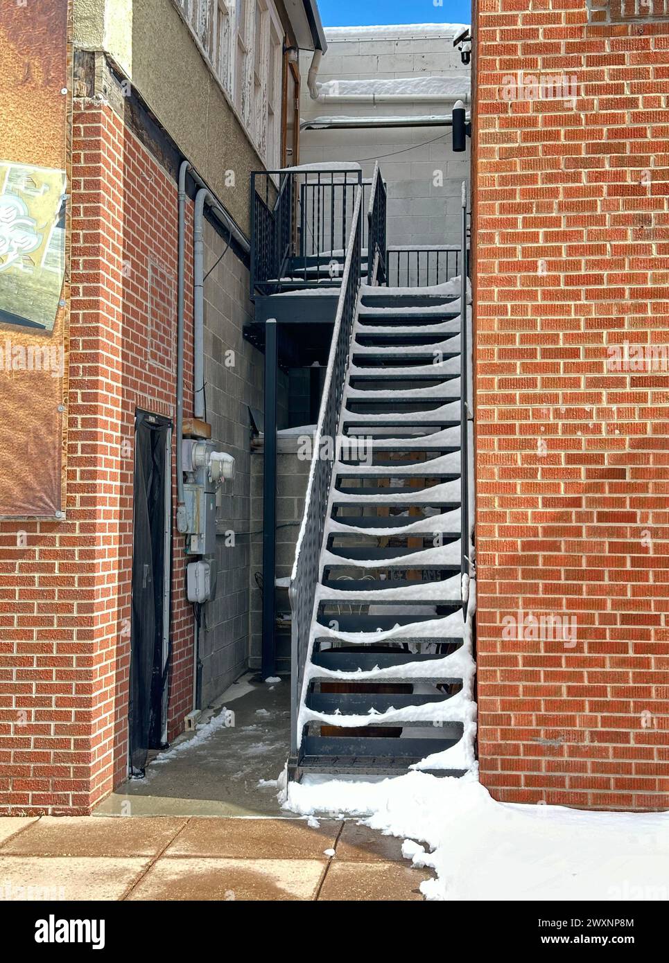 La scala esterna con neve conduce alla camera al piano superiore. L'edificio in mattoni rossi mostra una porta laterale d'ingresso. Si trova in un'area business. Foto Stock