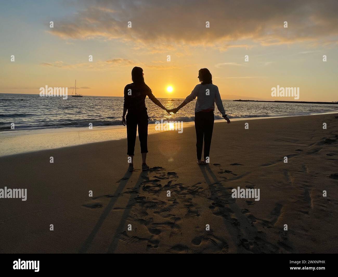 Un paio di persone che passeggiano mano nella mano su una spiaggia al tramonto Foto Stock Un paio di persone che passeggiano mano nella mano su una spiaggia al tramonto Foto Stock