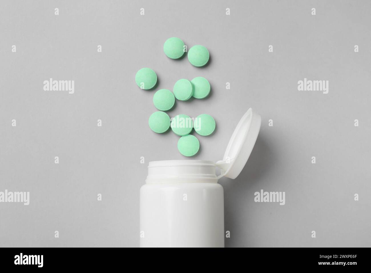 Pillole vitaminiche e bottiglia verde chiaro su sfondo grigio, vista dall'alto Foto Stock