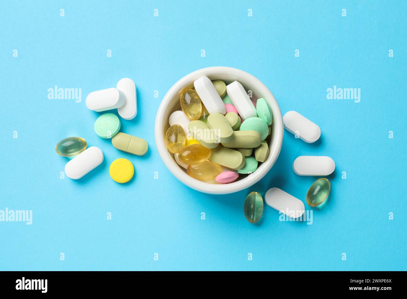 Diverse pillole vitaminiche nel recipiente su sfondo azzurro, vista dall'alto Foto Stock