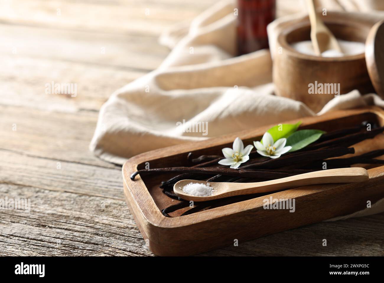 Baccelli di vaniglia, fiori, foglie e cucchiaio con zucchero su tavola di legno, primo piano. Spazio per il testo Foto Stock