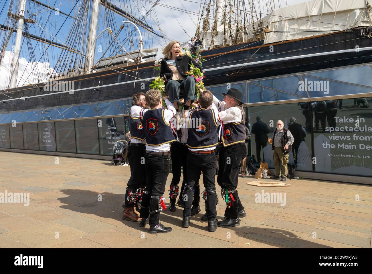 01/04//2024. Londra, Regno Unito. I membri del gruppo Blackheath Morris Dancers iniziano la stagione di danza Morris con un tradizionale evento di "Easter Chair lifting" fuori dal Cutty Sark a Greenwich. Una donna volontaria viene sollevata su una sedia decorata con fiori per celebrare la Pasqua. Crediti fotografici: Ray Tang Foto Stock