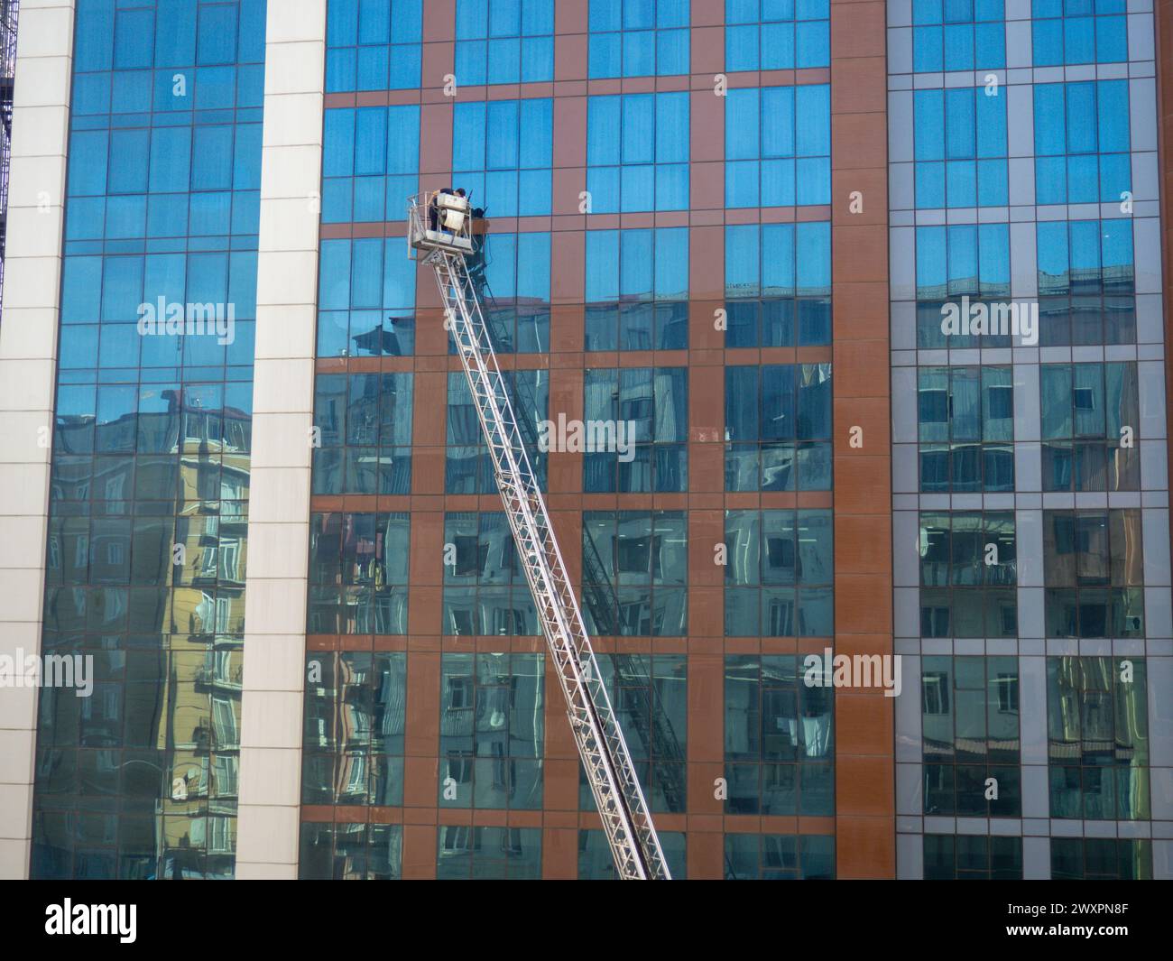 Pulizia delle finestre in un grande edificio di vetro. Lavorare in altezza su un sollevatore. Uomo in una culla. Industria moderna Foto Stock