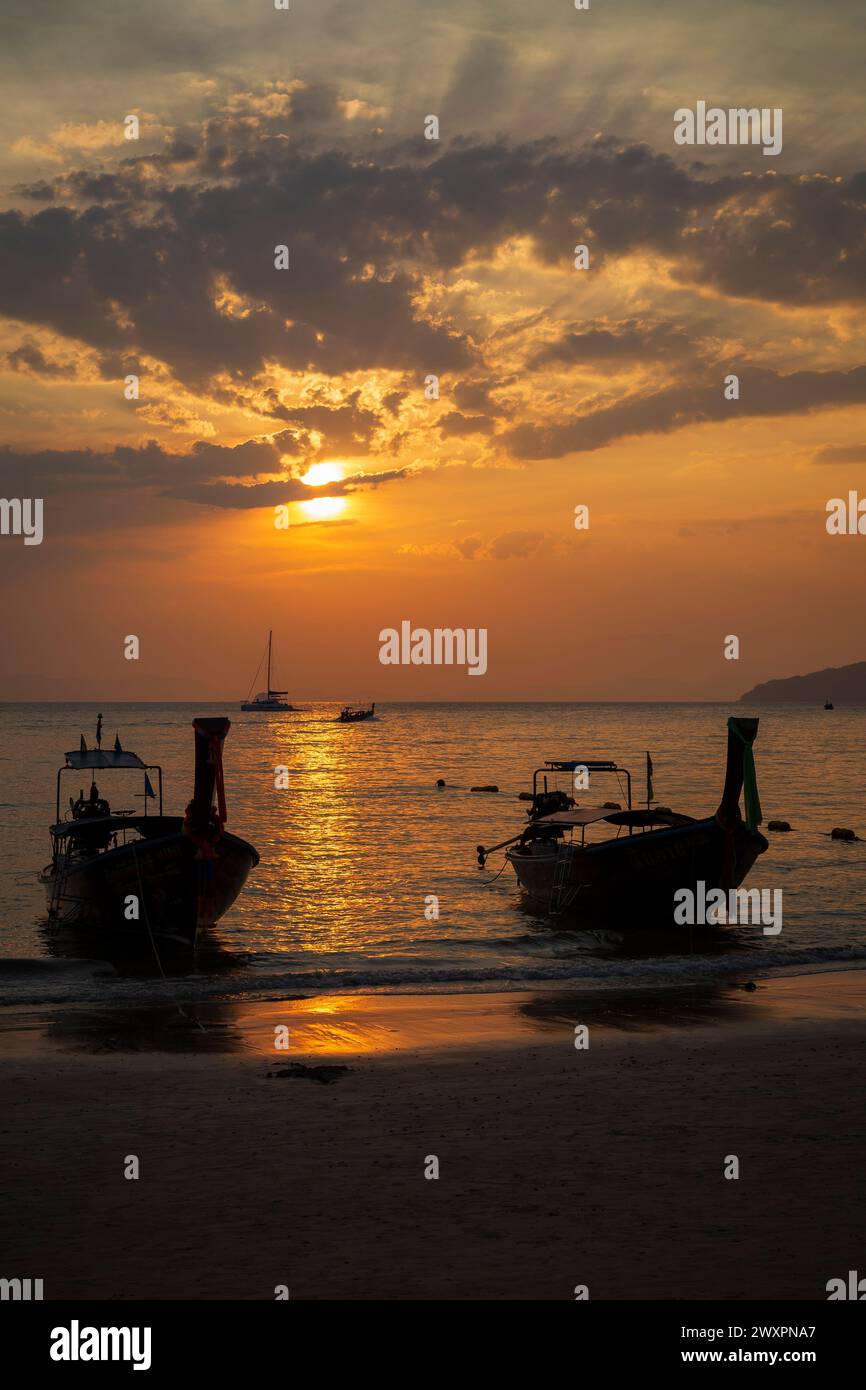 Splendida vista della silhouette delle barche a coda lunga, del mare e dello splendido cielo arancione durante il tramonto alla spiaggia di Railay West a Railay, Krabi, Thailandia. Foto Stock