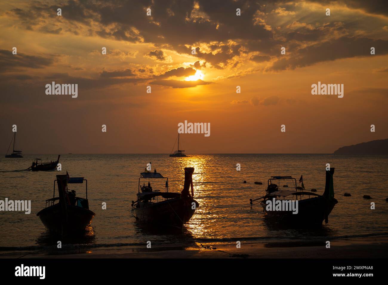Splendida vista della silhouette delle barche a coda lunga, del mare e dello splendido cielo arancione durante il tramonto alla spiaggia di Railay West a Railay, Krabi, Thailandia. Foto Stock
