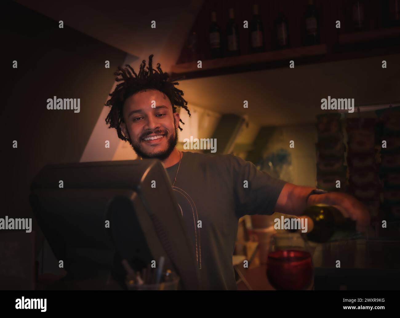 Giovane barista afroamericano che porge vino rosso in bicchiere e sorride Foto Stock