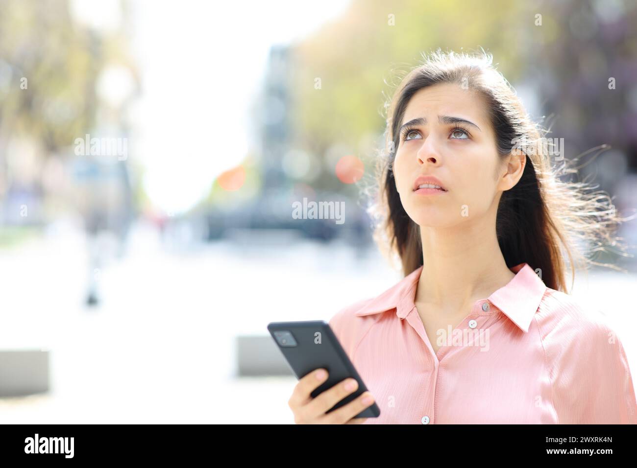 Donna preoccupata che usa il telefono per trovare un posto che guarda in alto in piedi per strada Foto Stock