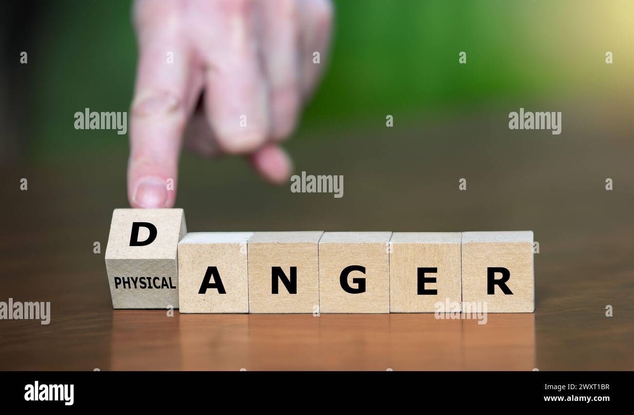 La mano gira il cubo di legno e cambia l'espressione "rabbia fisica" in "pericolo". Foto Stock