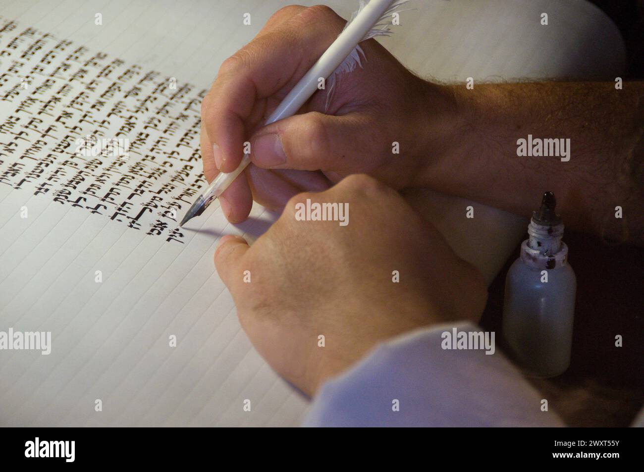 Vista ravvicinata delle mani di uno scriba ebreo che scrive il testo ebraico della Torah o della Bibbia su pergamena usando una trappola di piume e inchiostro nero. Foto Stock