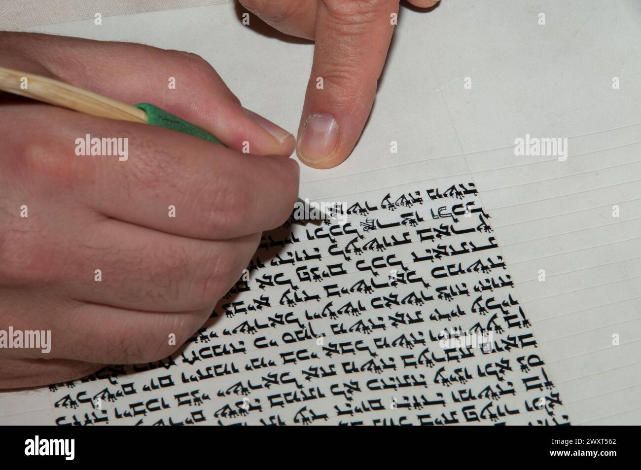 Vista ravvicinata delle mani di uno scriba ebreo che scrive il testo ebraico della Torah o della Bibbia su pergamena usando una trappola di piume e inchiostro nero. Foto Stock