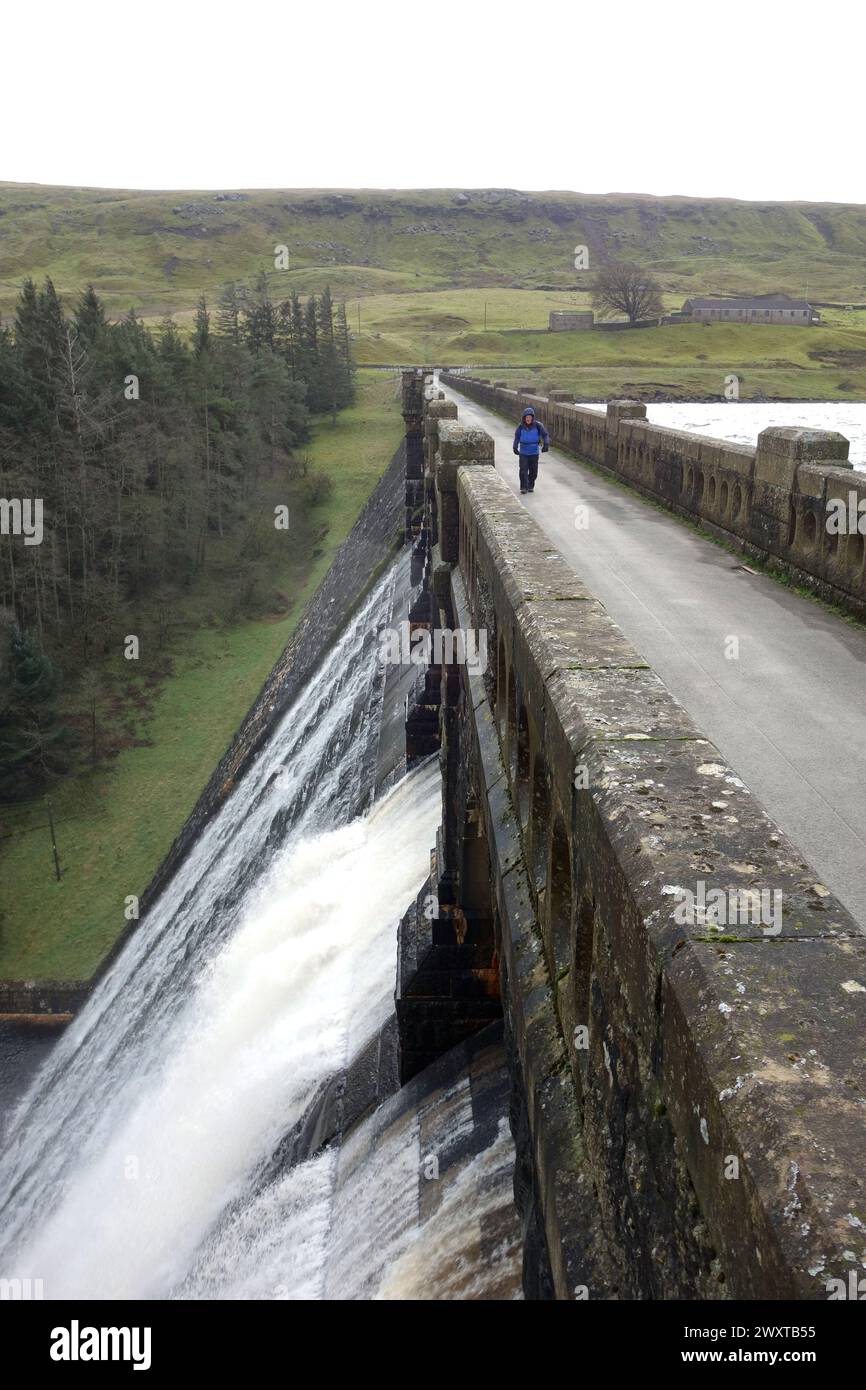 Man (escursionista) camminando sull'efflusso sul muro della diga di pietra di Scar House Reservoir a Nidderdale, Yorkshire Dales National Park, Inghilterra, Regno Unito. Foto Stock