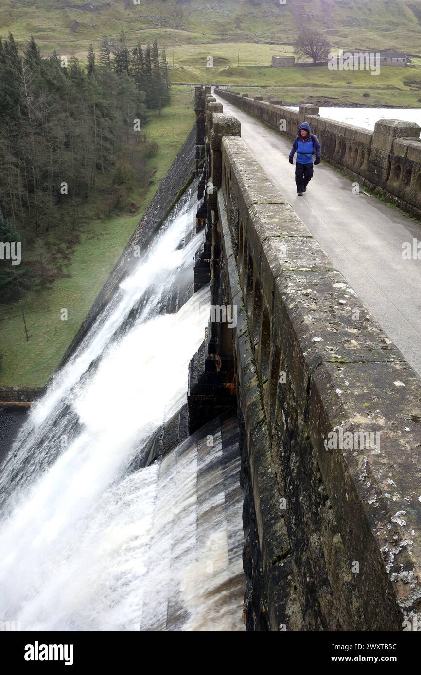 Man (escursionista) camminando sull'efflusso sul muro della diga di pietra di Scar House Reservoir a Nidderdale, Yorkshire Dales National Park, Inghilterra, Regno Unito. Foto Stock