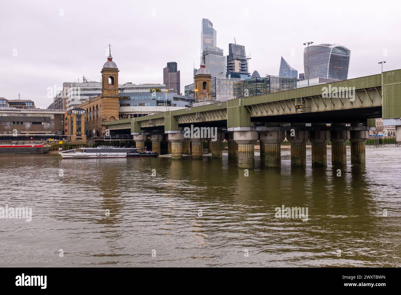 Una barca Uber sul fiume Tamigi scivola sotto il ponte ferroviario di Cannon Street con la stazione di Cannon Street e i grattacieli della città alle spalle. Foto Stock