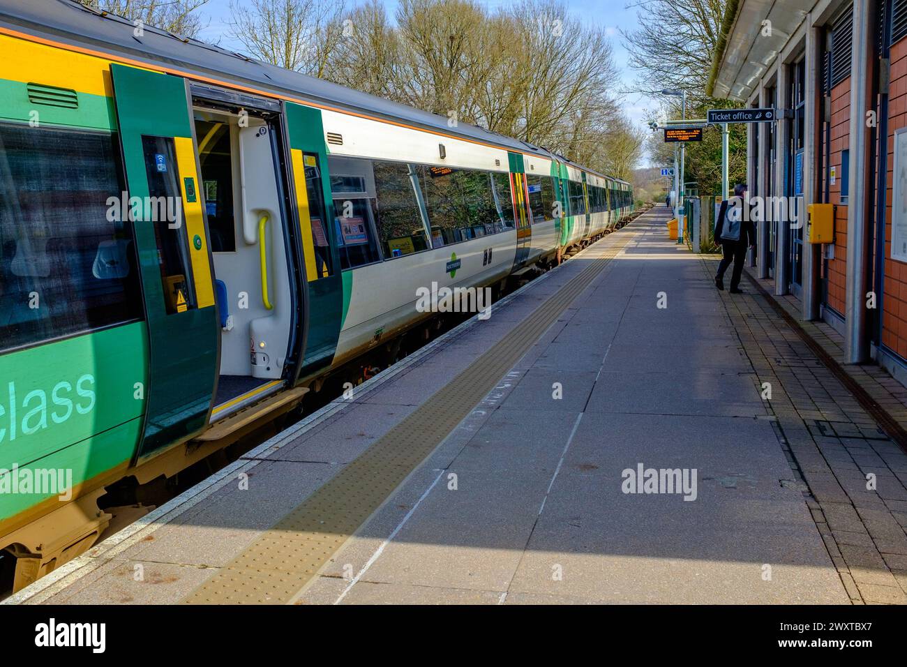 Un treno della Southern Railway in livrea verde e gialla si erge con le sue porte aperte sulla piattaforma della stazione quasi vuota Foto Stock