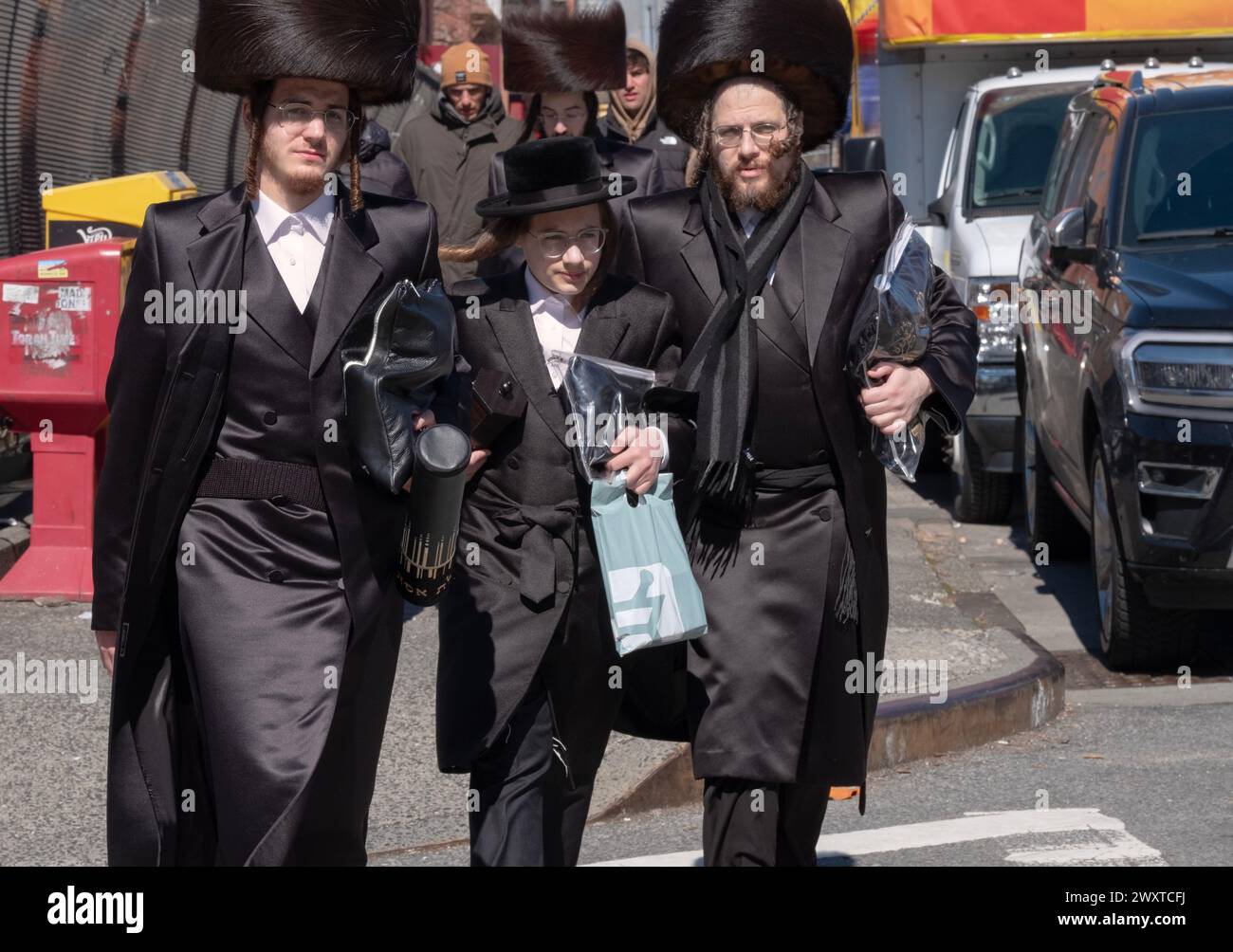 Uomini chassidici, alcuni indossano cappelli in pelliccia di shtreimel. Ritorno dai servizi mattutini di Purim vestiti con il meglio delle loro vacanze. A Brooklyn, New York. Forse la famiglia. Foto Stock