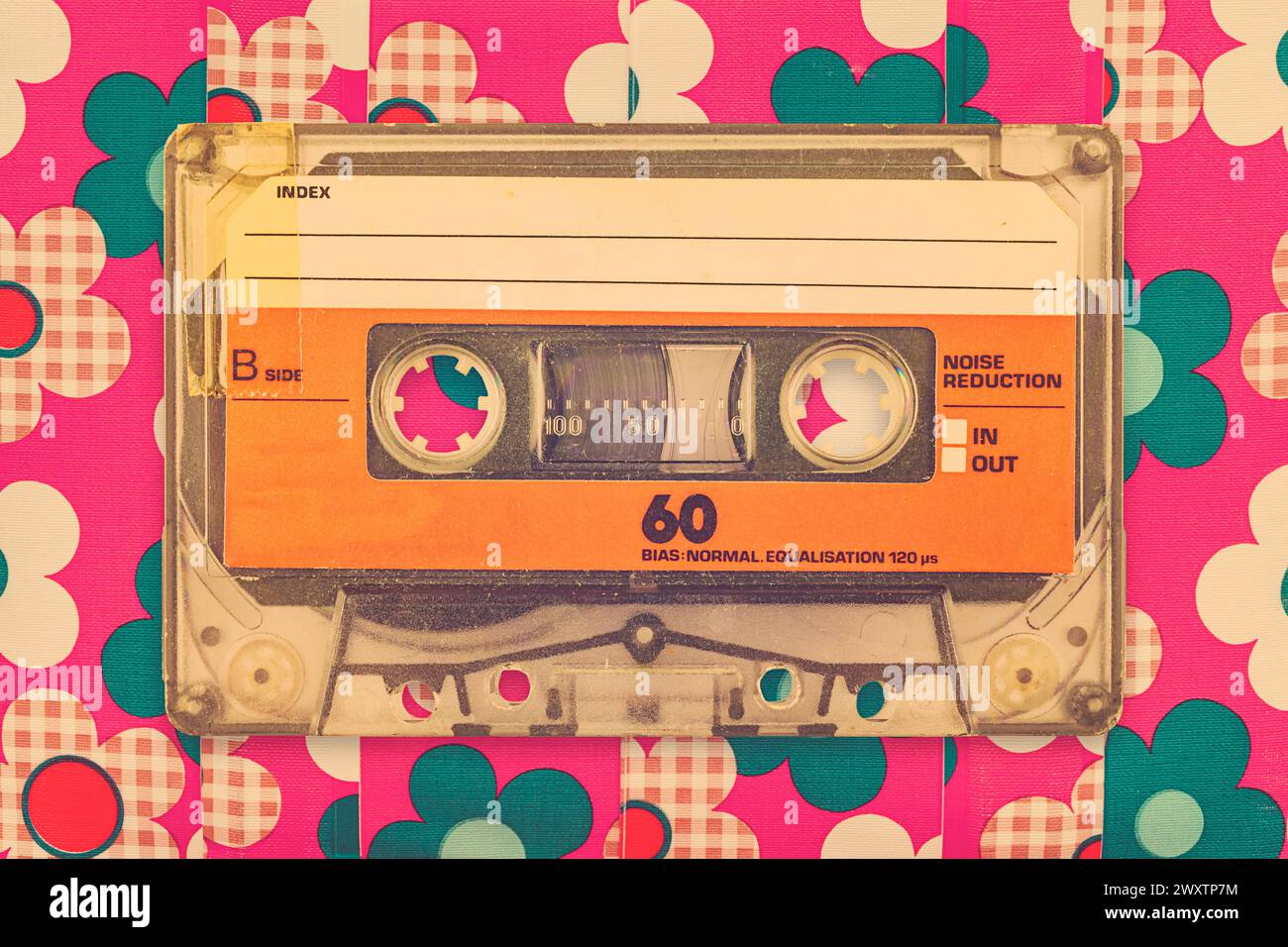 Cassetta audio compatta arancione vintage davanti a uno sfondo con motivo floreale Foto Stock