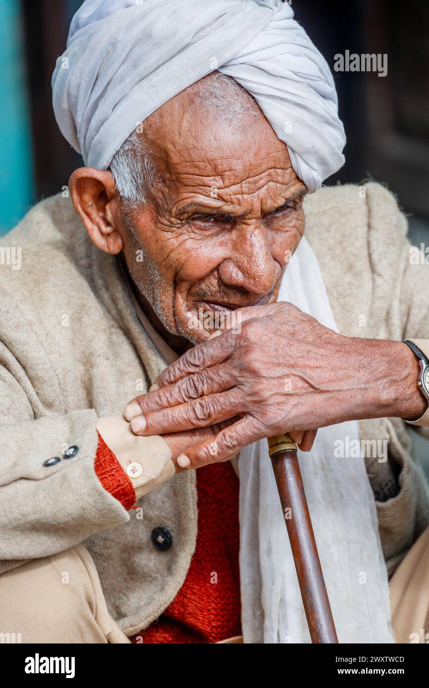 Anziano uomo locale che indossa un turbante che fuma un narghilè nel villaggio di Naddi View Point, famoso per le vedute dell'imponente catena montuosa di Dhauladhar Foto Stock