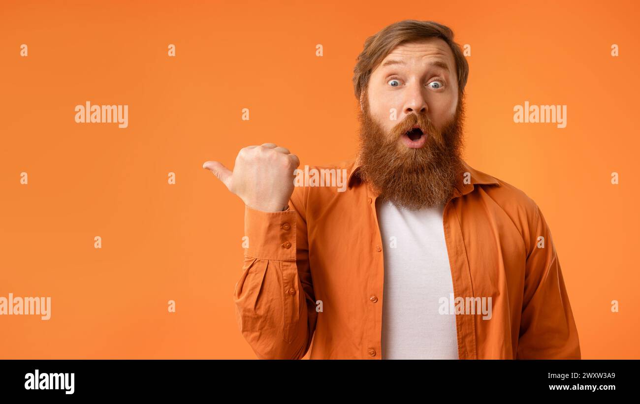 Uomo dai capelli rossi sorpreso con la barba che punta il dito del pollice da parte, studio Foto Stock