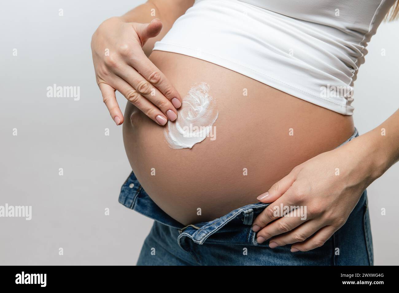 Donna incinta che applica crema idratante nella sua pancia grande Foto Stock