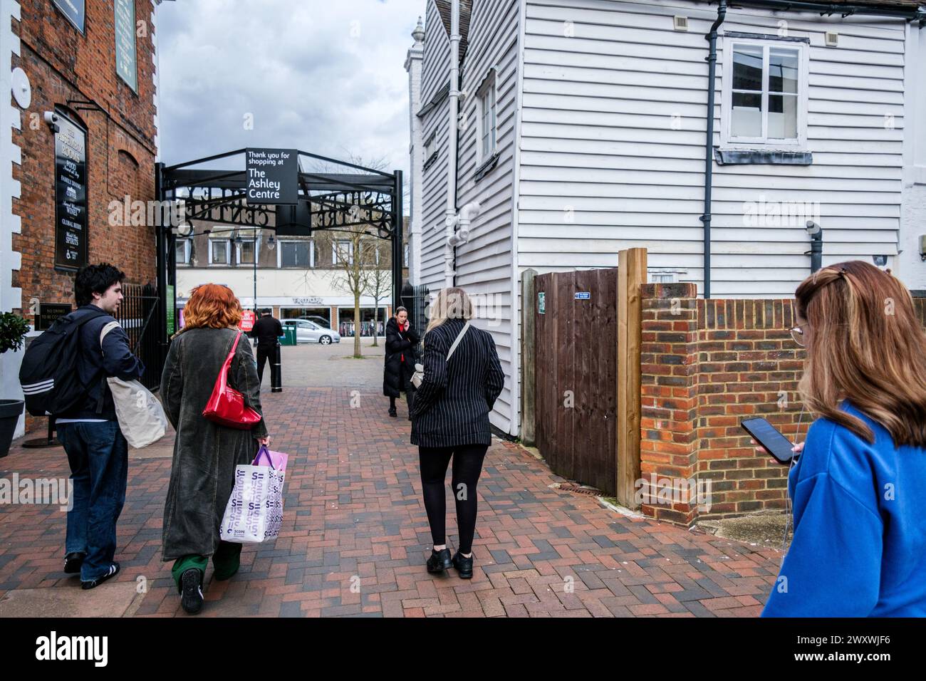 Epsom Surrey, Regno Unito, 02 aprile 2024, Small Group of People Carry Shopping Bags Walking Woman Using a Mobile Phone texting Foto Stock