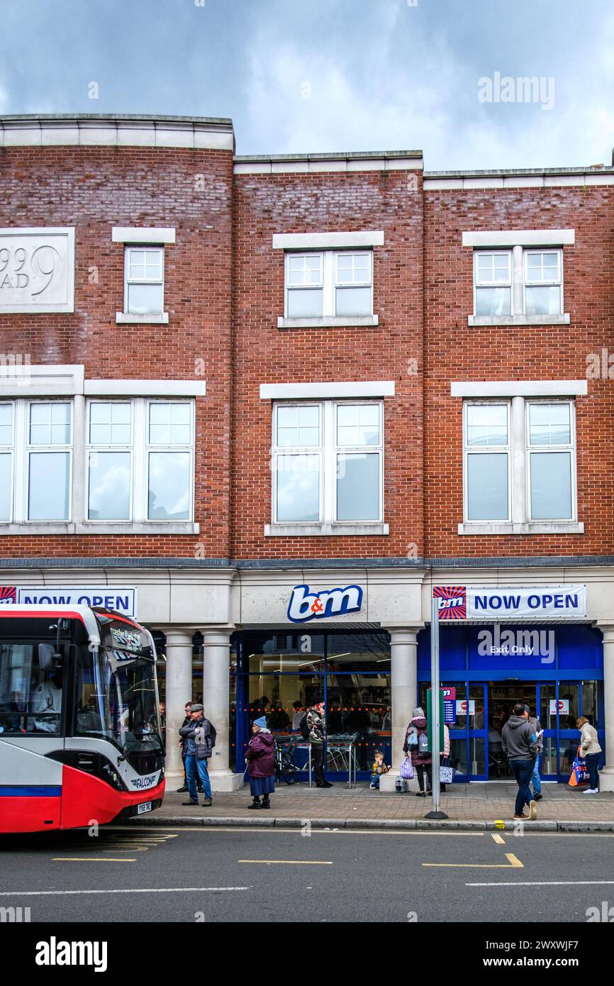 Epsom Surrey, Regno Unito, 02 aprile 2024, B&M Discount Shop with People or Shoppers Oside e Un autobus Falcon a un piano con cancelleria parcheggiata Foto Stock