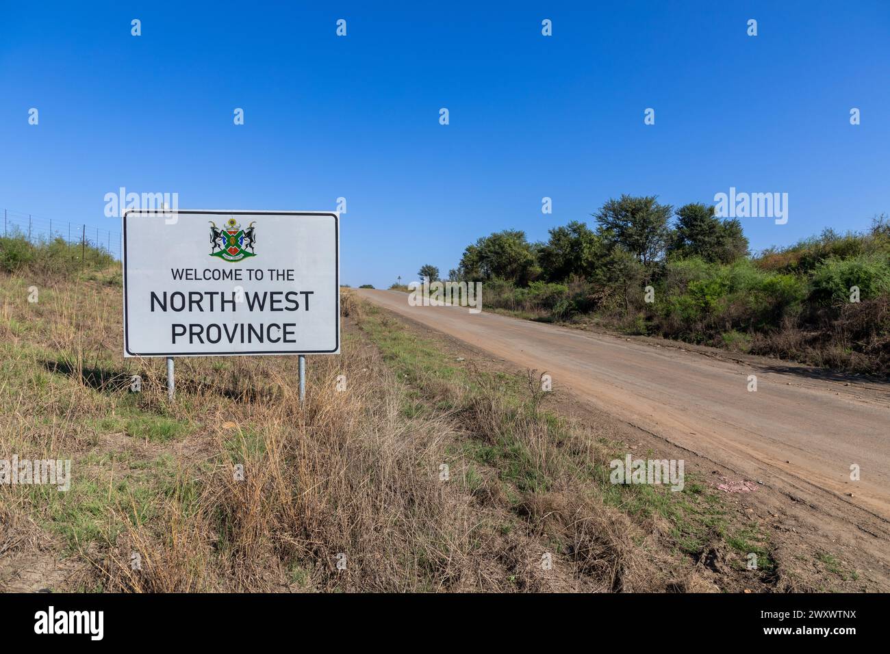 Paesaggio di una strada sterrata con un cartello che indica Benvenuti nella provincia nord-occidentale vicino a Stilfontein. Foto Stock