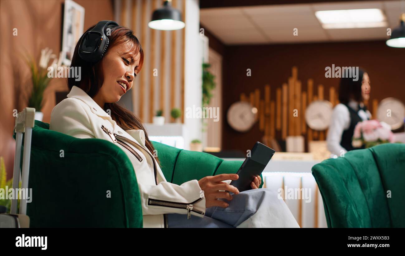 Viaggiatore che utilizza un tablet per passare il tempo nella sala dell'hotel, guardare film o cercare luoghi da visitare durante il soggiorno. Donna asiatica che naviga su pagine Internet, concetto di turismo. Scatto a mano libera. Foto Stock