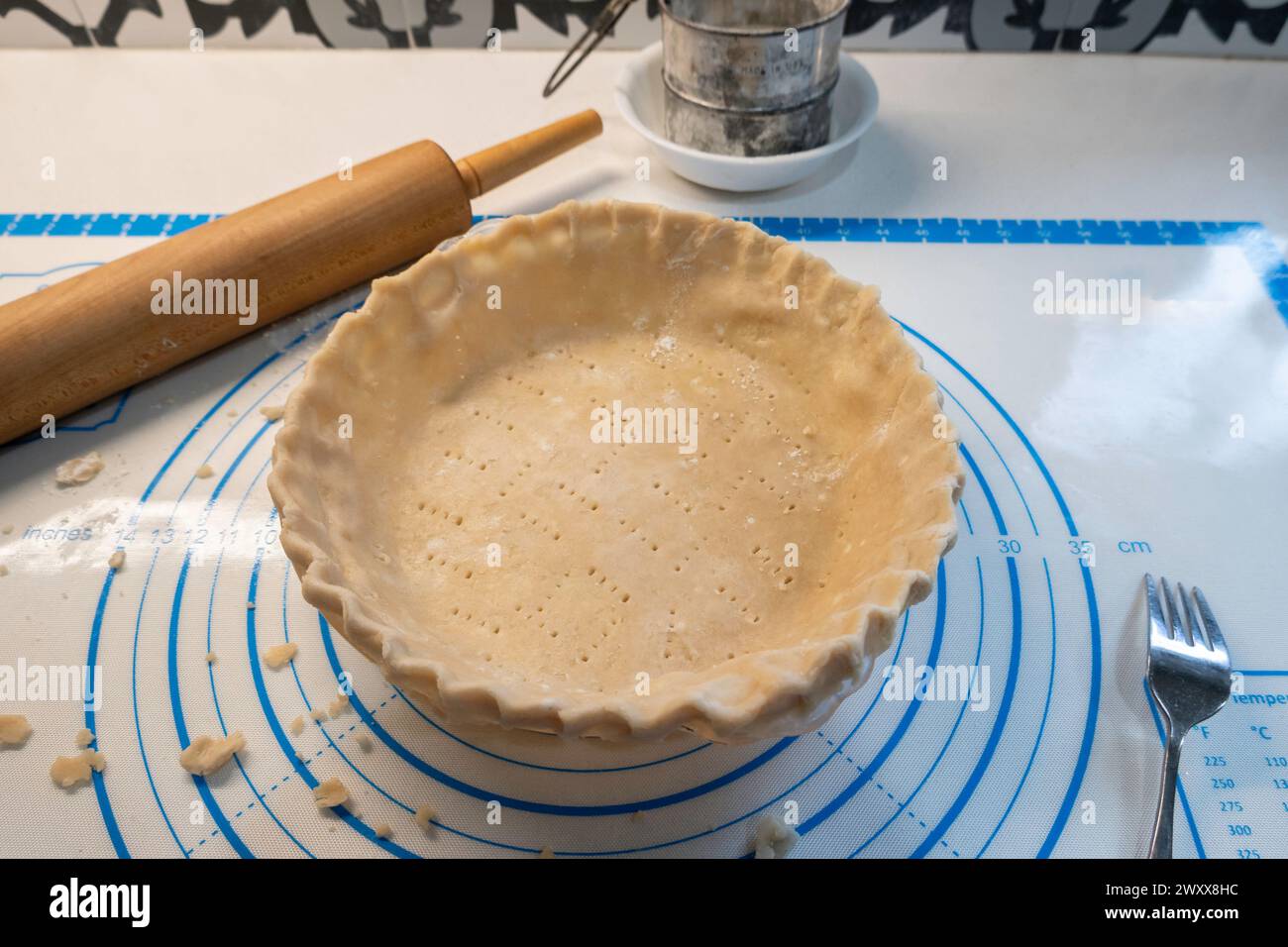 Crosta per torte o pasta sfogliata e inserita in un piatto per torte. Setaccio farina e mattarello in legno visibili. Foto Stock
