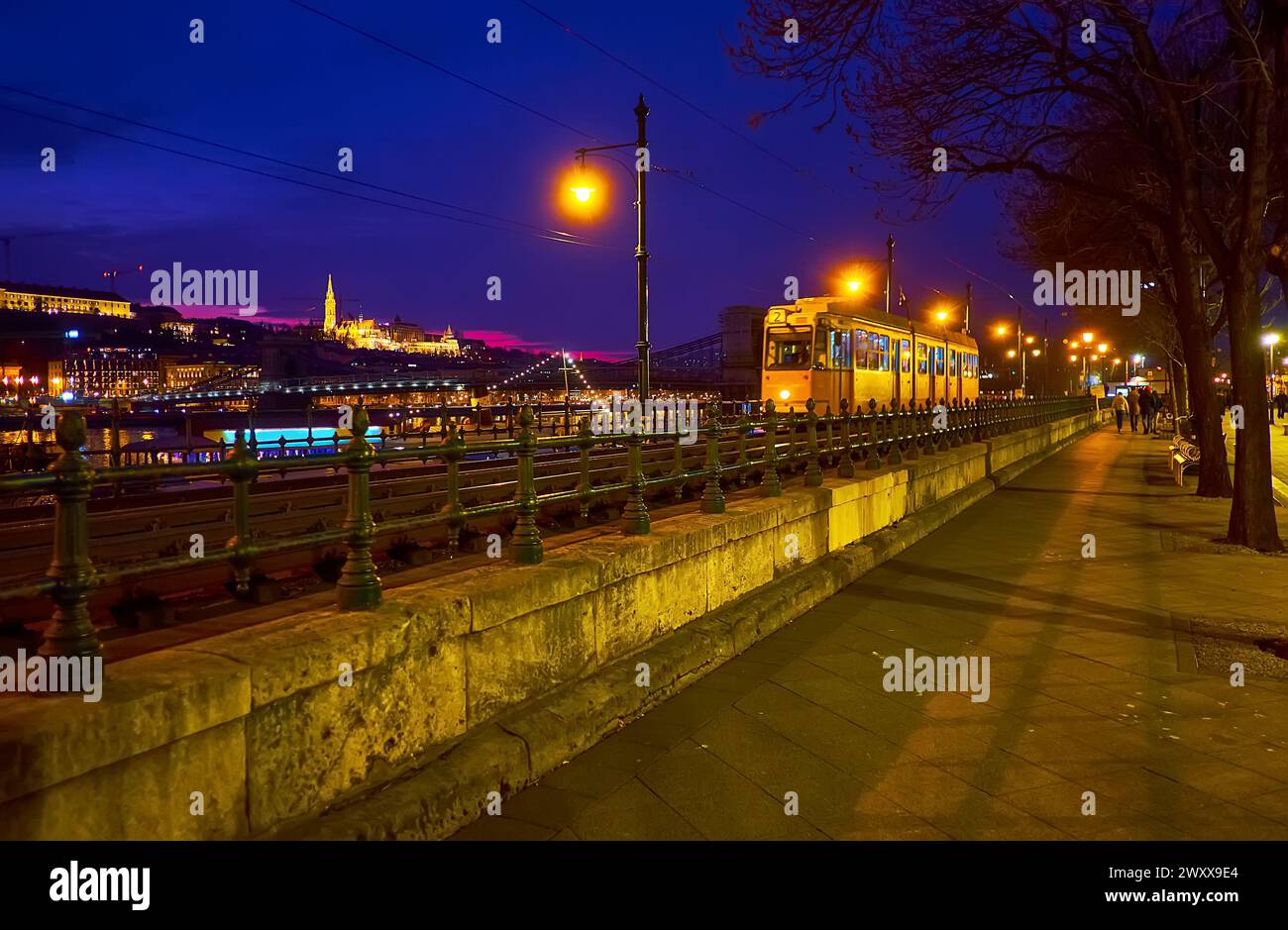 Il tram, percorrendo la sera Jane Haining Quay sullo sfondo del Bastione dei pescatori, situato sul lato opposto della riva del Danubio, Budapest, H. Foto Stock