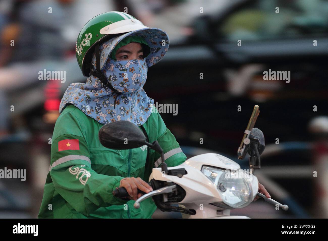 "Grab" - un'app di consegna - donna mascherata, su uno scooter, vista laterale nel traffico, ho chi min City (Saigon), Vietnam marzo 2024 Foto Stock